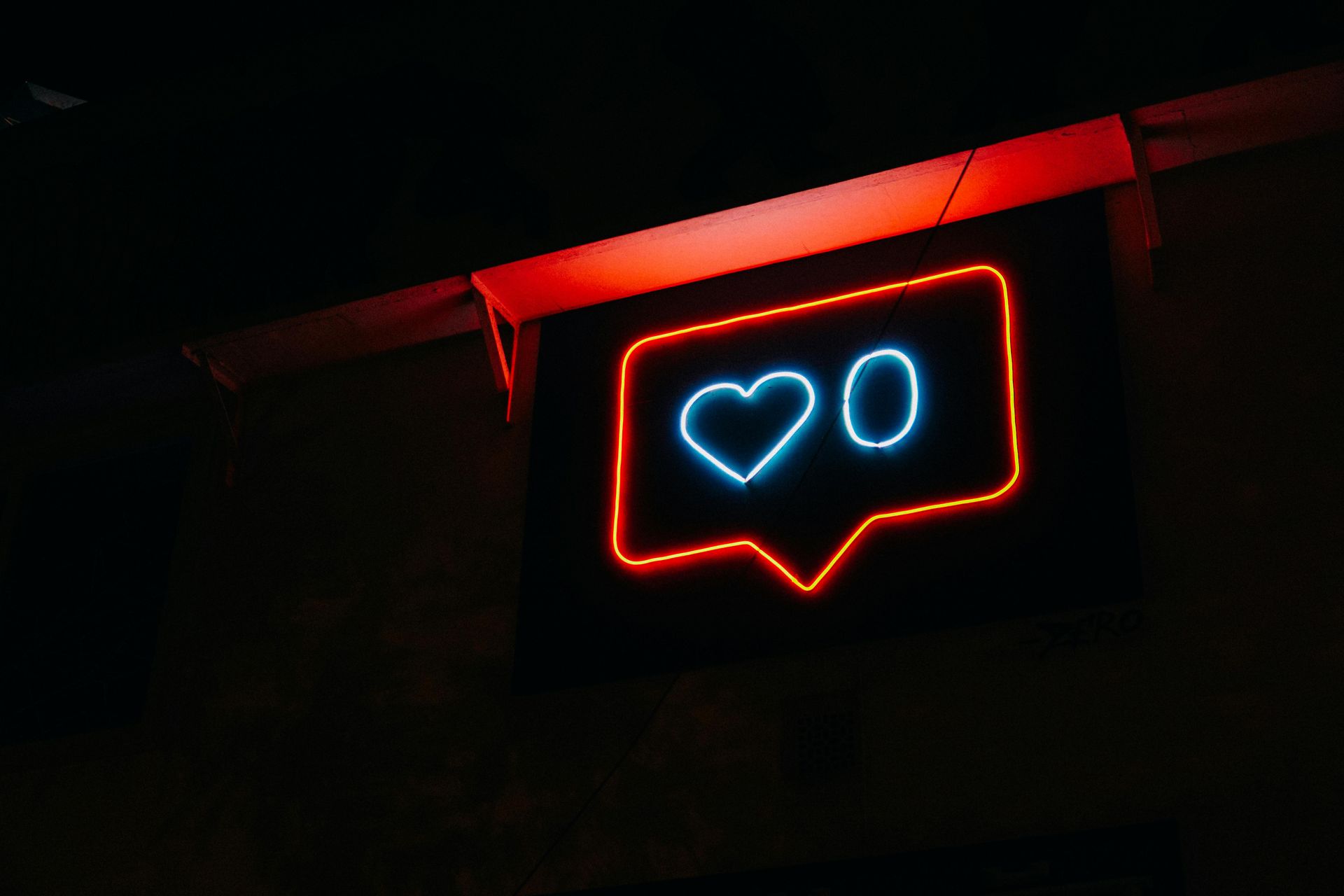 Illuminated neon sign with a heart and speech-bubble icon glowing at night